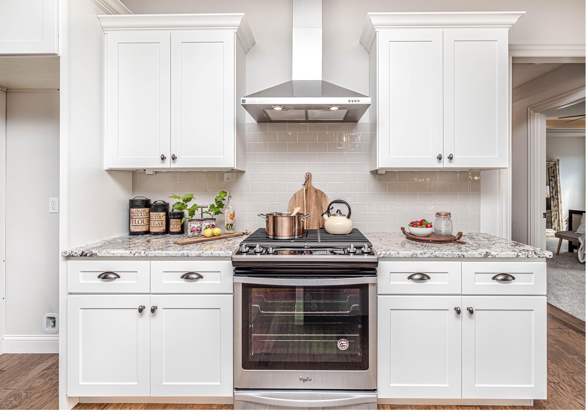 freshly painted white kitchen cabinets flanking stainless gas top range with marble countertops