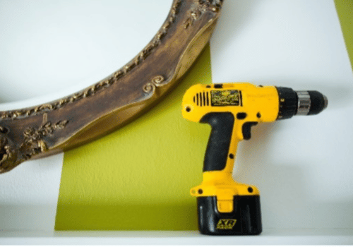 Yellow power drill in front of old wooden mirror frame
