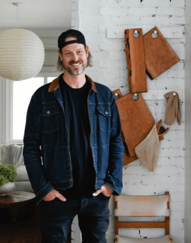 Steve ford wearing black baseball cap and blue jean jacket over black shirt with hands in pockets smiling at camera