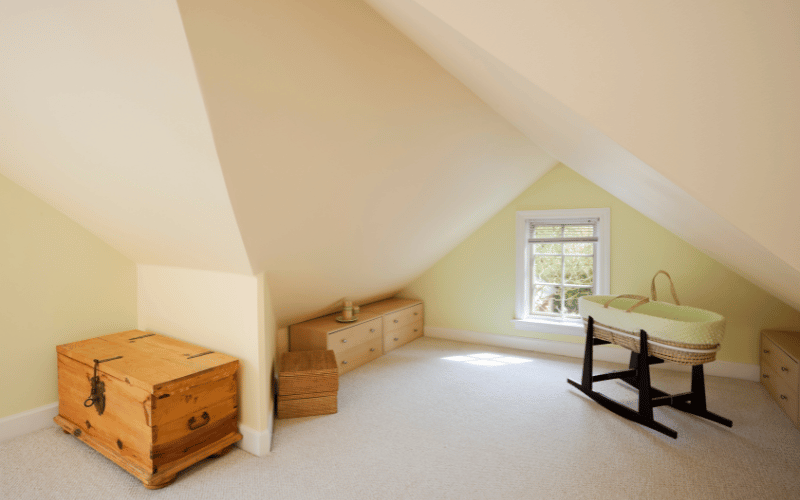 Clean and decluttered attic with muted yellow walls set up as a nursery