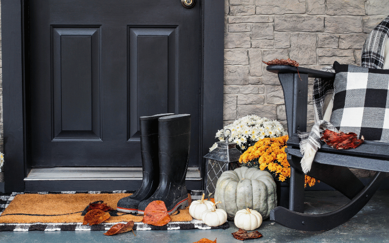 Front porch with black door, black rain boots, mini white pumpkins and orange mums plus a black and white plaid porch blanket