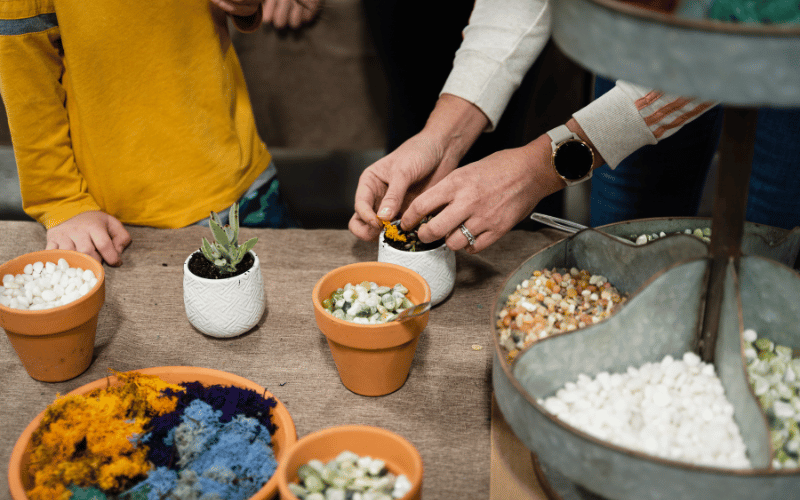close up of hands and arms of adult and child making their own terrarium in workshop.