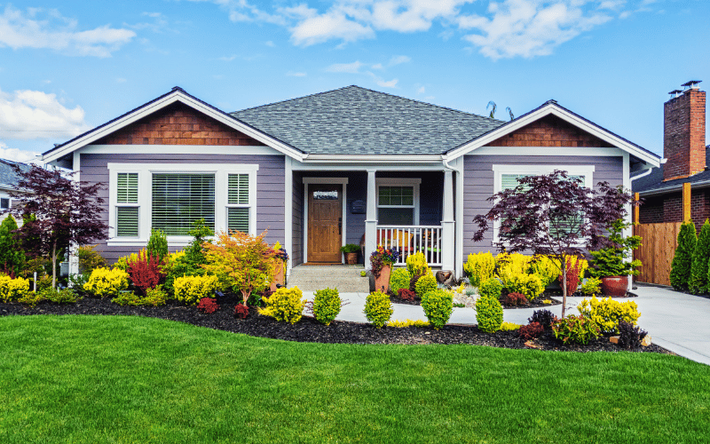 Light purple modular home with well maintained green grass and garden and white front porch