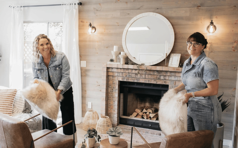 Lyndsay Lamb and Leslie Davis fluffing furry pillows in farm house rustic living room