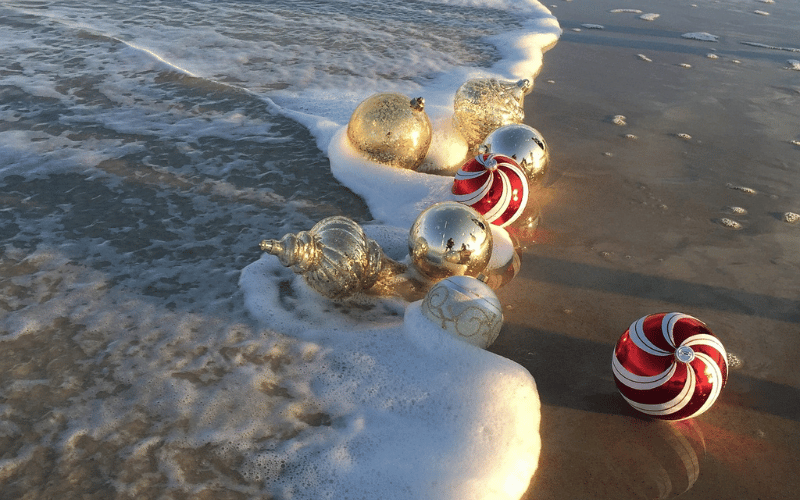 Large Christmas ornaments being washed onto sandy shore by waves