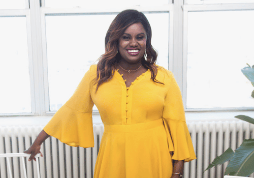 Celebrity Ati Williams wearing bright yellow dress posing and smiling in front of window