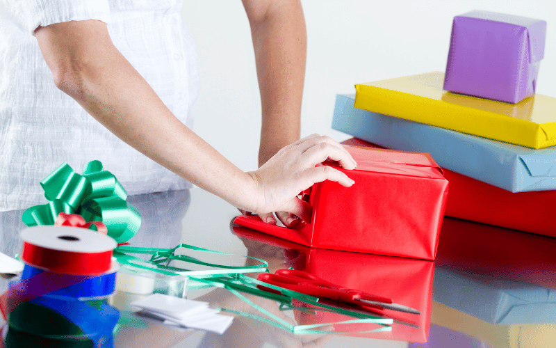 Person gift wrapping several large boxes on table. 