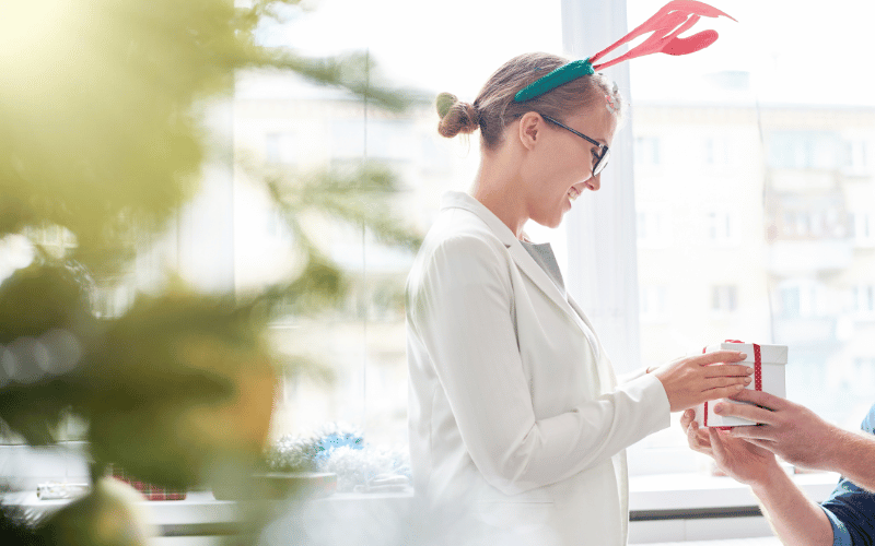 women in white shirt wearing Christmas antlers receiving white gift box