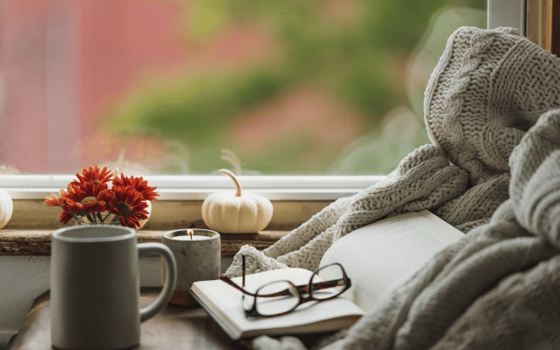 Reading nook with hot drink glasses, white pumpkin decor, red mum and grey warm blanket