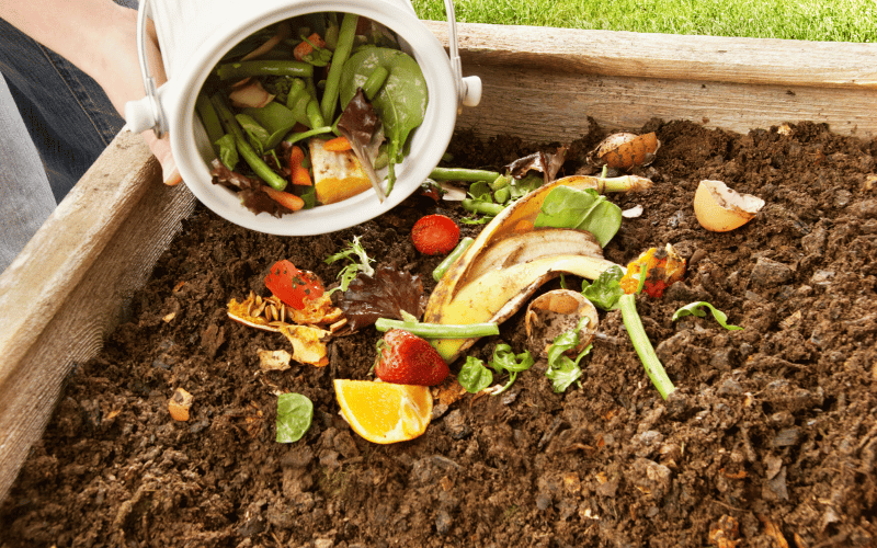 Male hands dumping ceramic white compost bin into outdoor large square compost pile