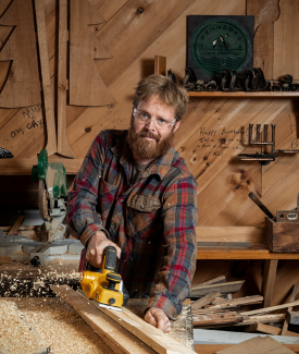 Chase Morrill Chase Morrill from Maine Cabin Masters Sanding a Wooden Beam in a Workshop