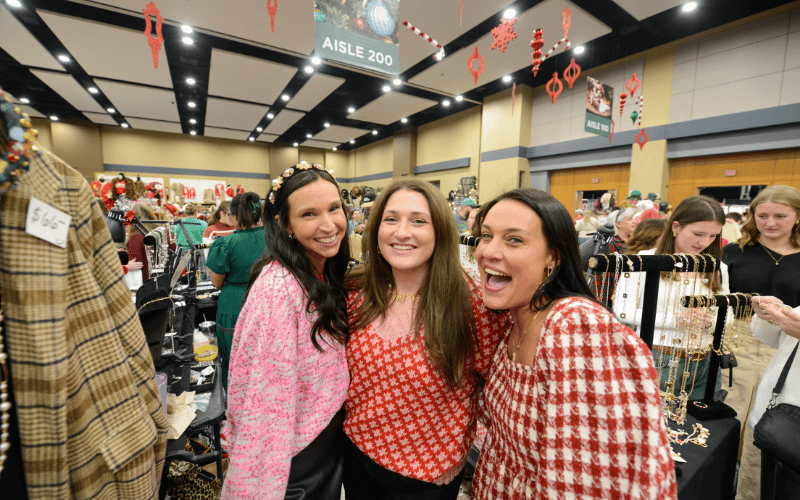 Three 20-30-something caucasian pretty brunette women smiling together at the KC Holiday Boutique