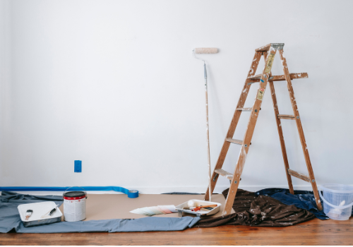 freshly painted white wall with ladder, paint roller and paint can on hardwood floor