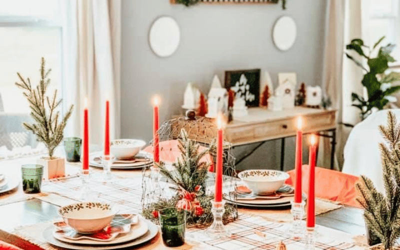 A table with bright red candles in the centre and fir sprigs in small pots 