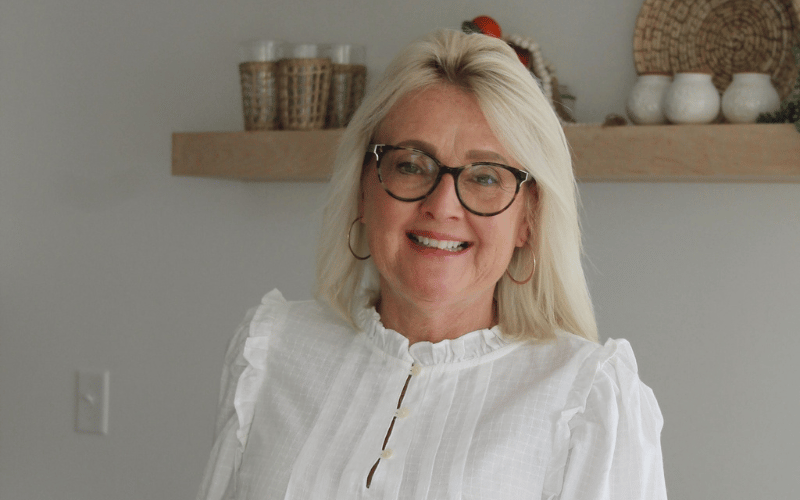 A woman posing in front of a floating shelf wearing glasses 