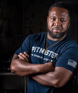 Ryan Mitchell posing wearing a pitmaster navy blue tshirt with crossed arms