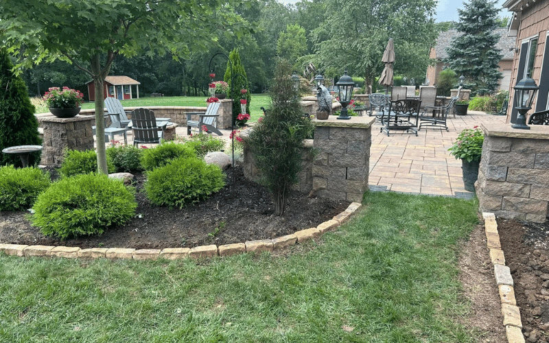 Backyard with green grass and shrubs along with hardsacped brick path and columns