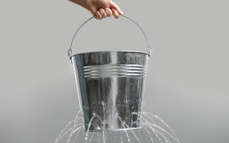 Silver garden bucket with lots of little leaks pouring water from it.